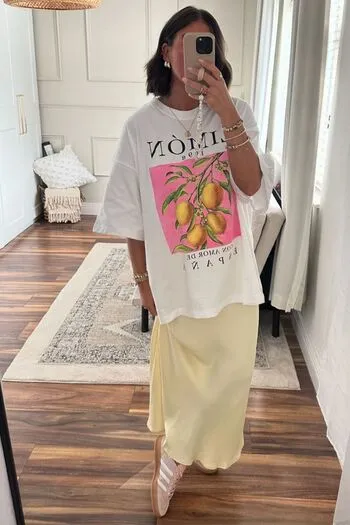 Homem usando camiseta tropical no verão colorida com estampa floral, combinada com bermuda bege e tênis branco, em um ambiente ensolarado de verão.