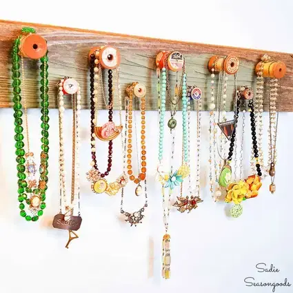 A colorful upcycled jewelry organizer ideas made from repurposed wooden frames and fabric, displaying necklaces and earrings on a rustic table.