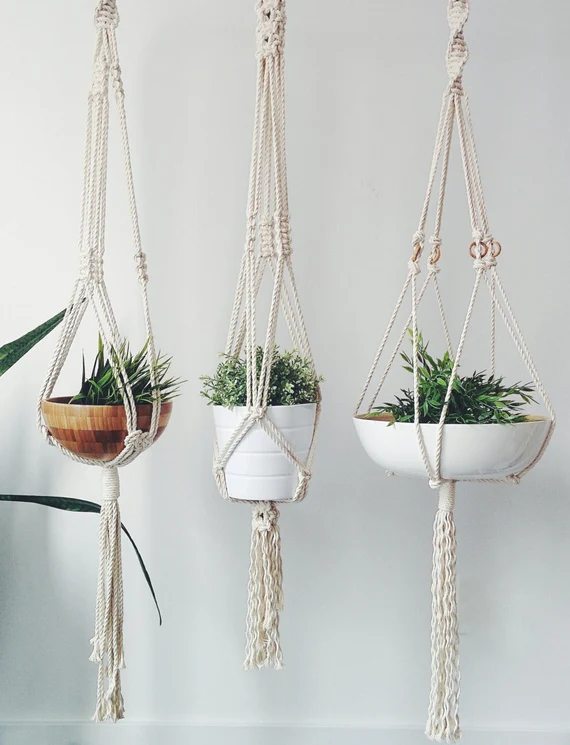 A diy macrame plant hangers with white cotton cord, featuring square knots and a wooden ring, holding a small ceramic plant pot against a neutral background.